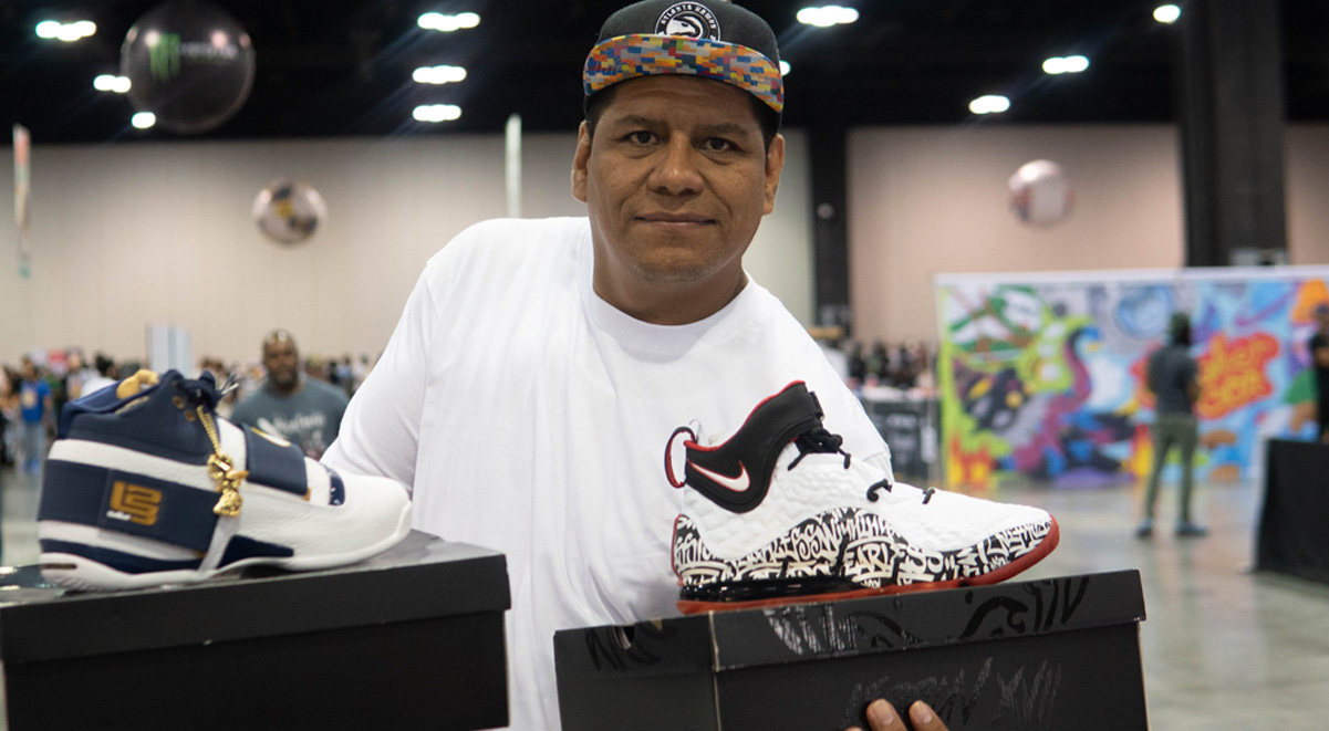 guy wearing a white shirt and cap posing with two basketball sneakers he bought 